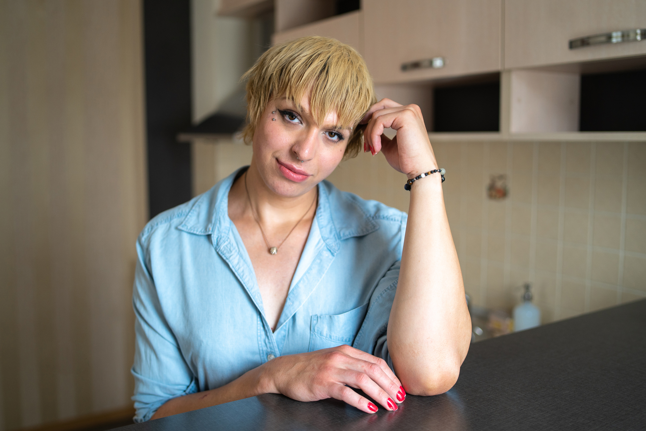 A young adult woman sitting at a desk with her left hand lightly touching her head.