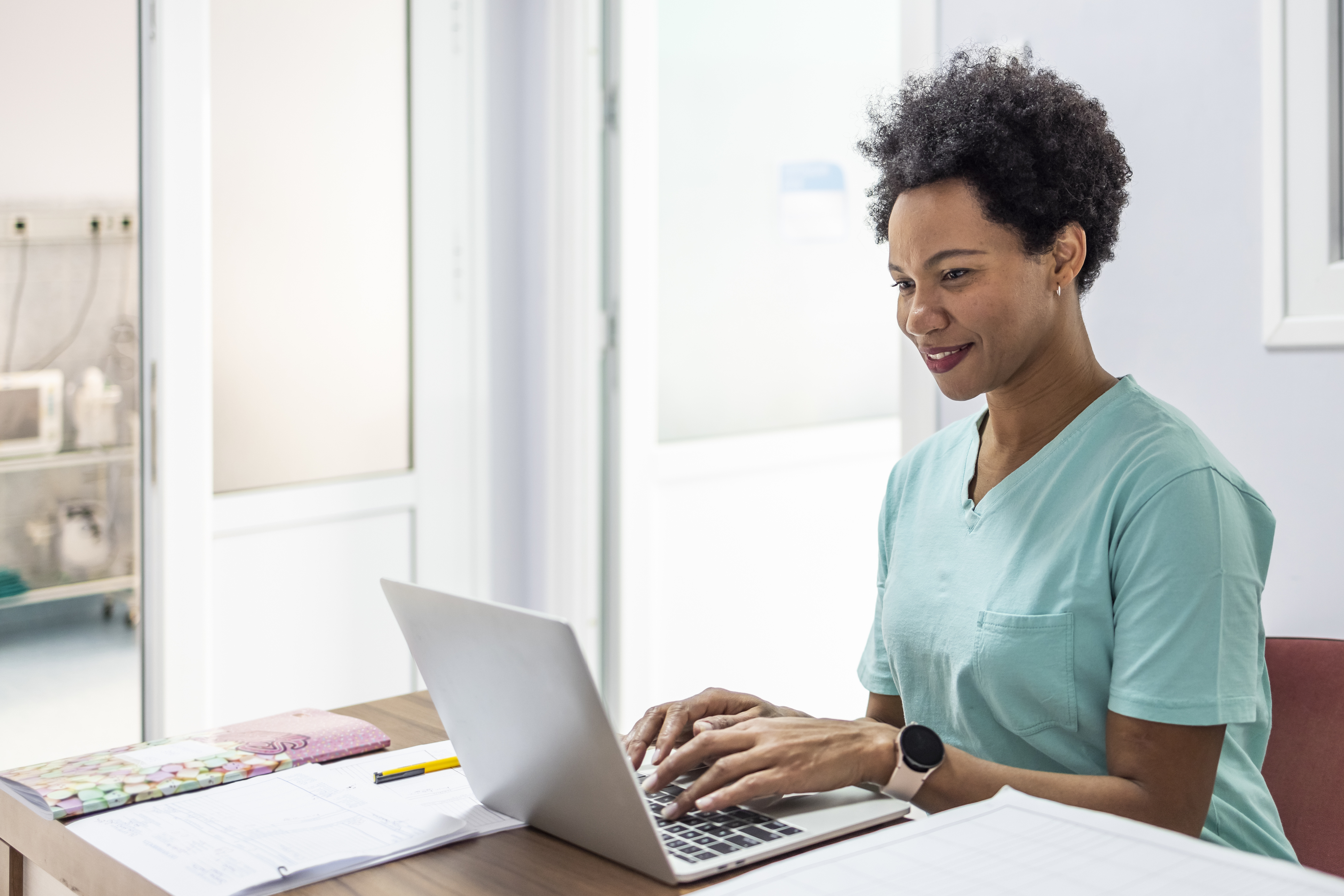 A healthcare professional typing on a laptop.