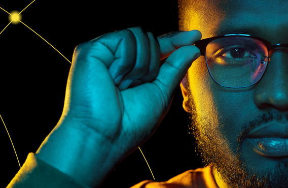 A close up of half a man's face with his right hand touching his glasses lens frame.