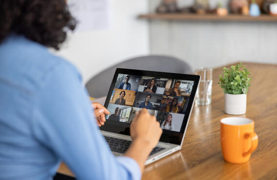 A woman sitting at a table, attending an online conference call on her computer.