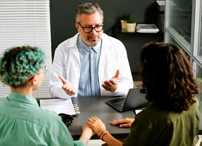 A doctor sitting with two patients discussing something.
