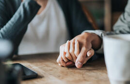 Two hands holding on a wooden table.